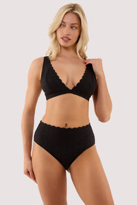 Model wears a nikki black broderie scallop high apex bikini top with a matching high leg brazilian bikini brief.