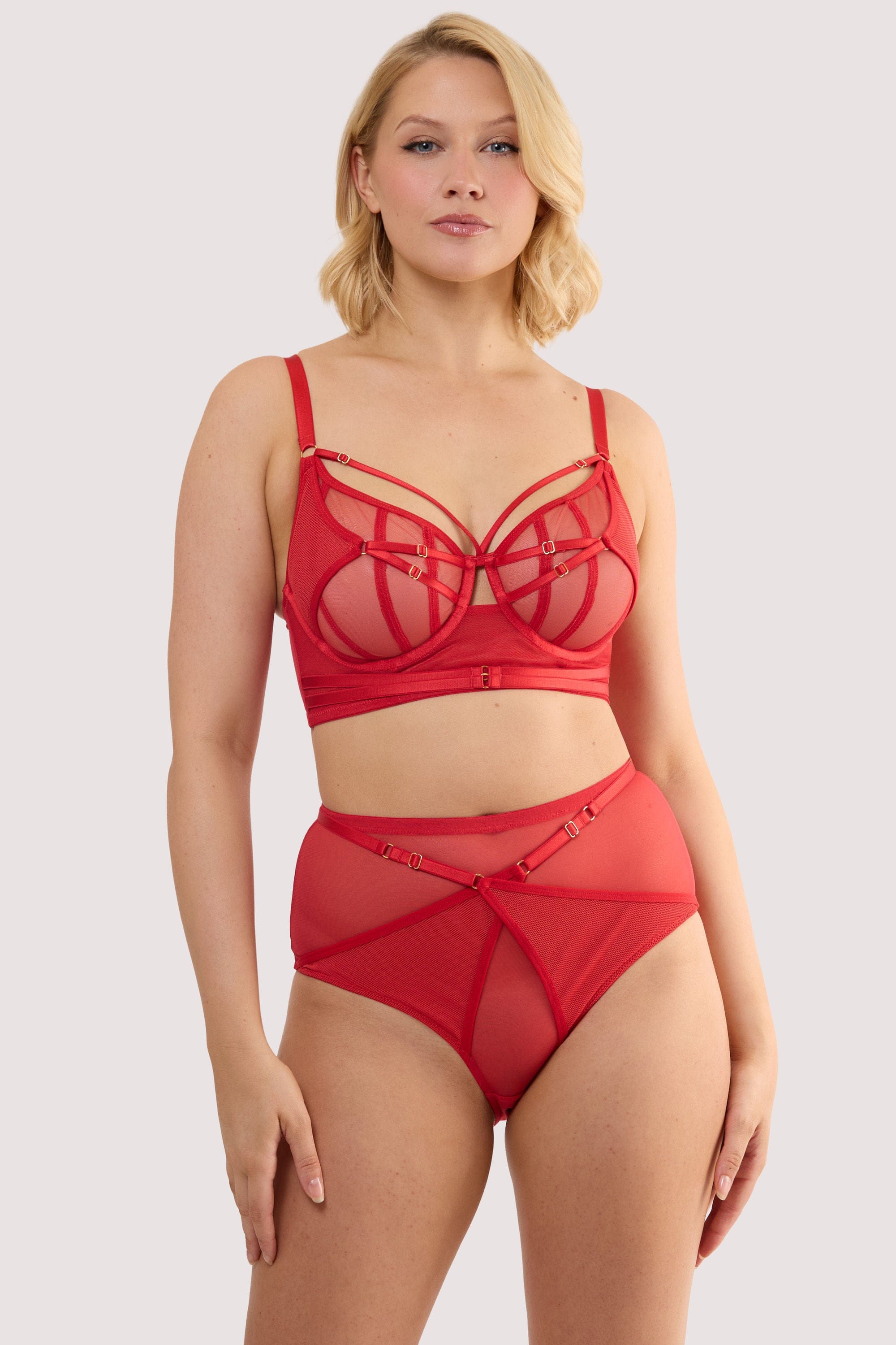 Model wears a eddie ruby red crossover high waist brief with ruby red mesh and fishnet panels, with a matching bra.