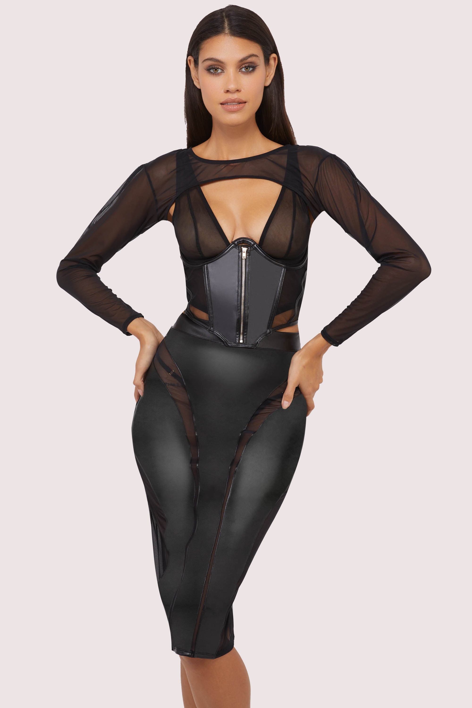 Model wears a black vegan leather mesh insert pencil skirt featuring leather panels with sheer mesh inserts with waist cinching, silhouette defining fit, with a matching shrug and underbust corset.