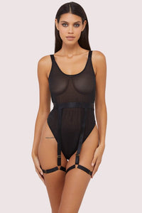 Model wears a black thick strap bodysuit with a semi sheer supportive mesh and adjustable thigh harness suspender.