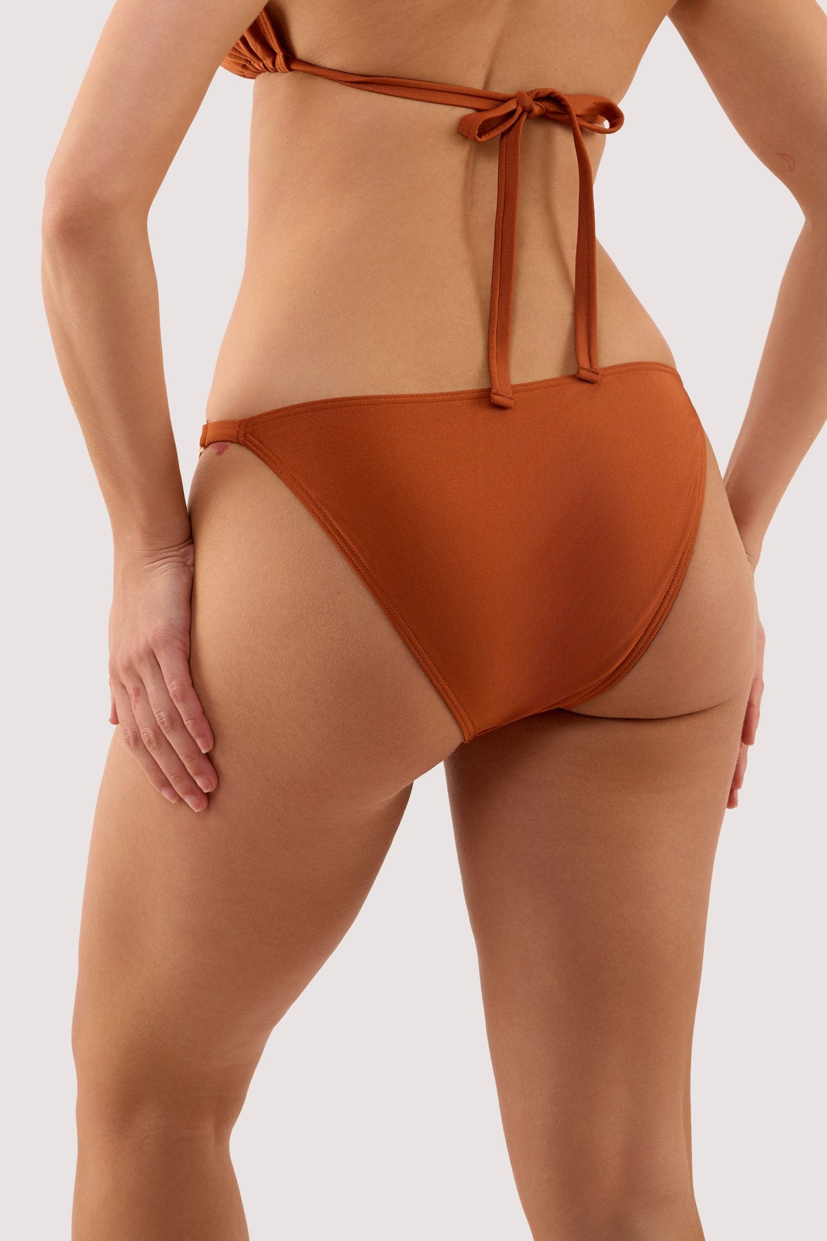 Model shows the back of a georgia brown high shine tie side bikini brief with hardwear.